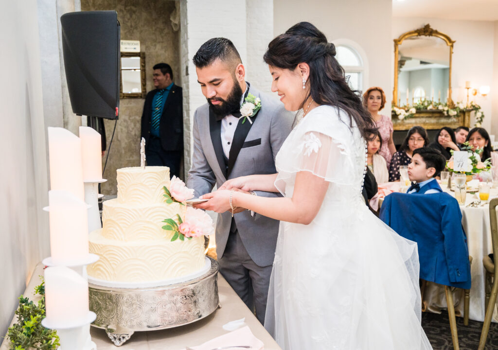 Couple cutting wedding cake at Grand Ballroom at Ceresville Mansion featuring chandeliers, tall ceilings, and elegant gold accents for wedding receptions.