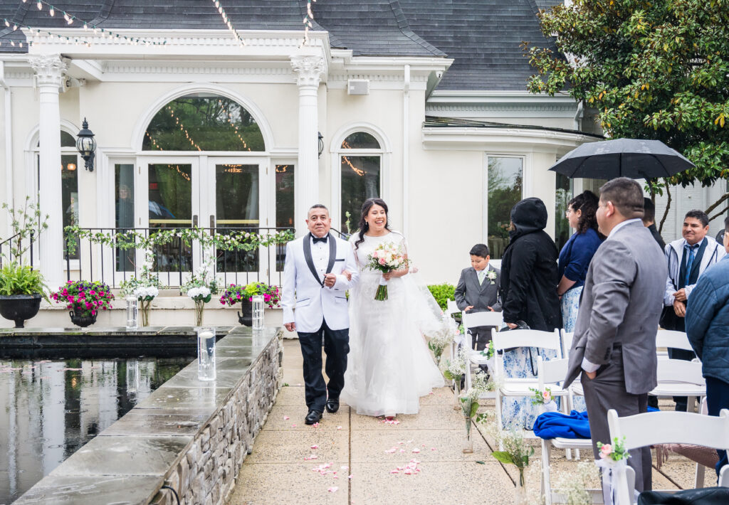 Bride walking down the aisle for wedding ceremony on the Garden Terrace at Ceresville Mansion surrounded by lush greenery.